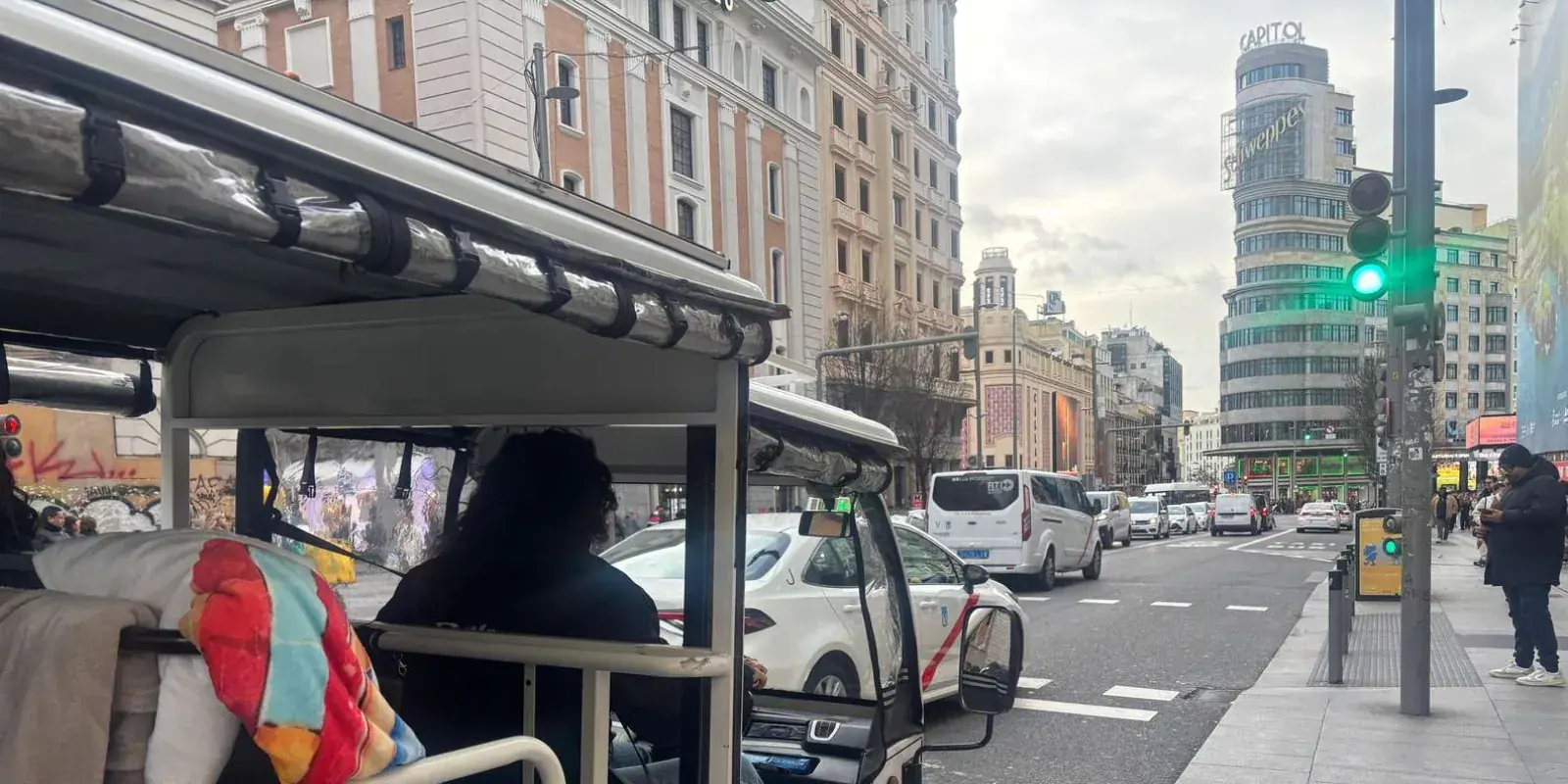 Tuk tuk with a passenger beside a Madrid avenue