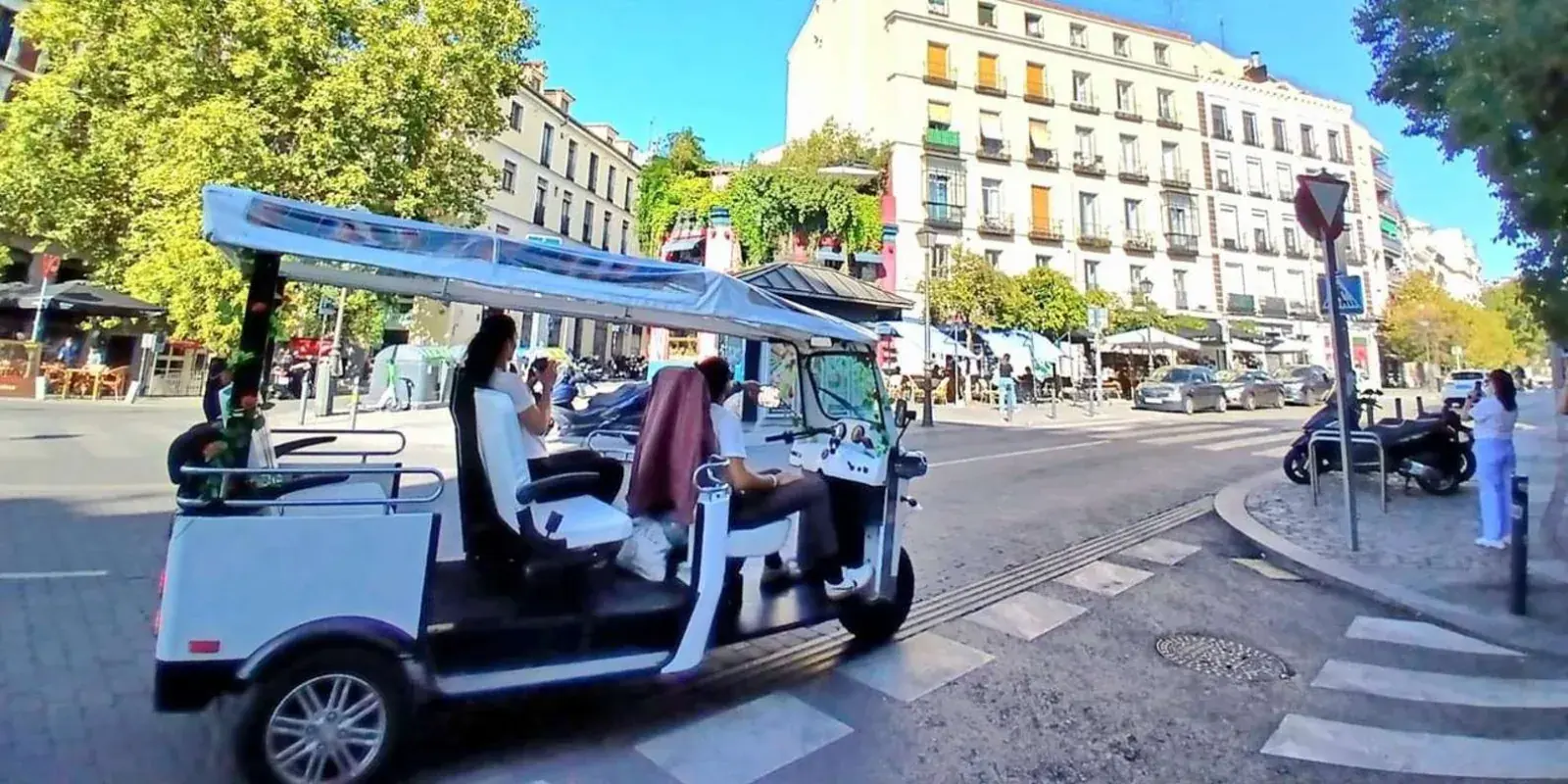 White tuk tuk travelling along a tree-lined avenue